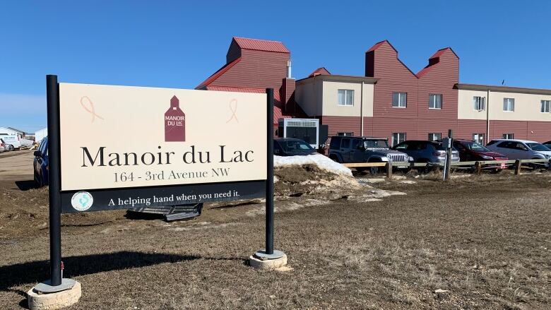 A red brick building with a small parking lot in front. A sign in front of the property reads, Manoir du Lac.