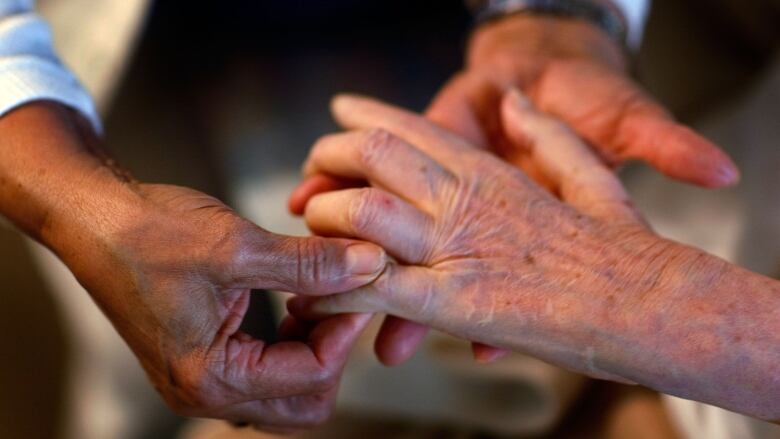 A closeup photo of a home health aide's hands massaging a senior's fingers.  