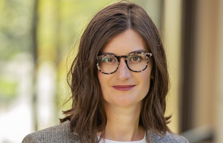 A woman with long brown hair and glasses smiles at the camera.