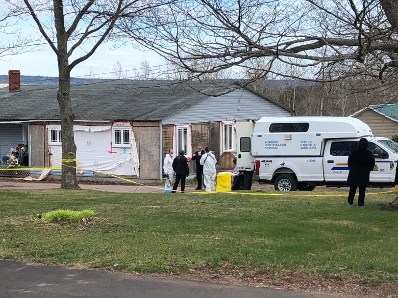 A home without siding surrounded by yellow police tape and police officers, some in hazmat suits. 