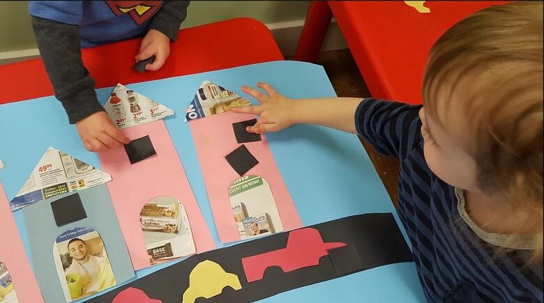 Two children in daycare play with coloured cutouts.