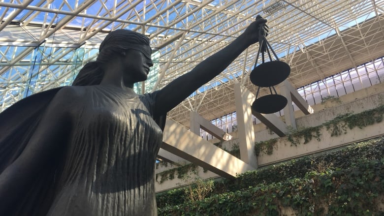 The scales of justice statue at B.C. Supreme Court with greenery and the buildings skylight roof in the background.