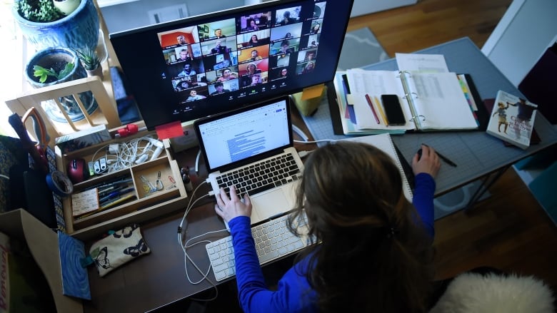 A woman works at a home work station desk, with a Zoom meeting on her computer screen.