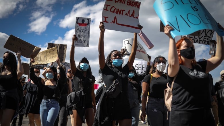 A group of masked protester hold up signs, on saying 