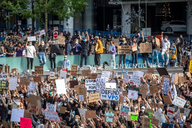 Dozens of people hold up signs reading 'Defund the VPD' and 'All Black Lives Matter', among other signs, at a giant rally.