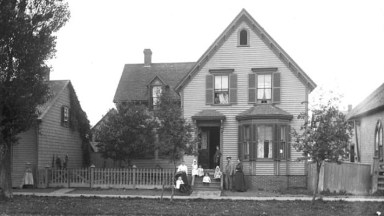 A black and white photo of a house on Kent Street in Charlottetown next door to The Bog School, which was located on the corner of Rochford and Kent streets in with residents of The Bog posing out front. 