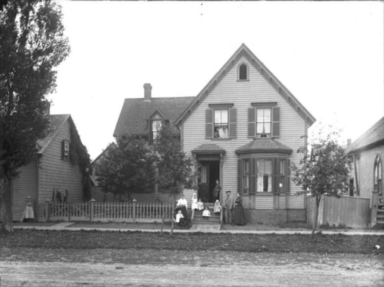 A black and white photo of a house on Kent Street in Charlottetown next door to The Bog School, which was located on the corner of Rochford and Kent streets in with residents of The Bog posing out front. 