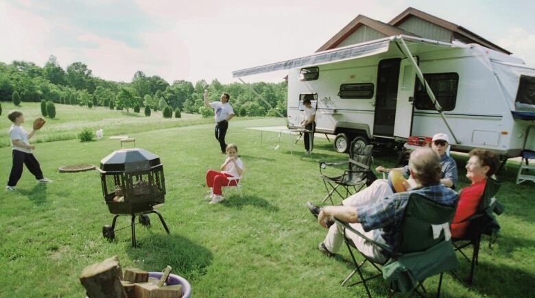 A trailer is set up on a grassy spot, with people of all ages enjoying themselves. 