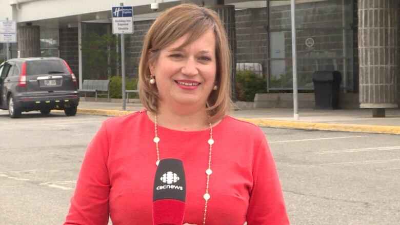 A woman wearing a red shirt stands outside an airport.