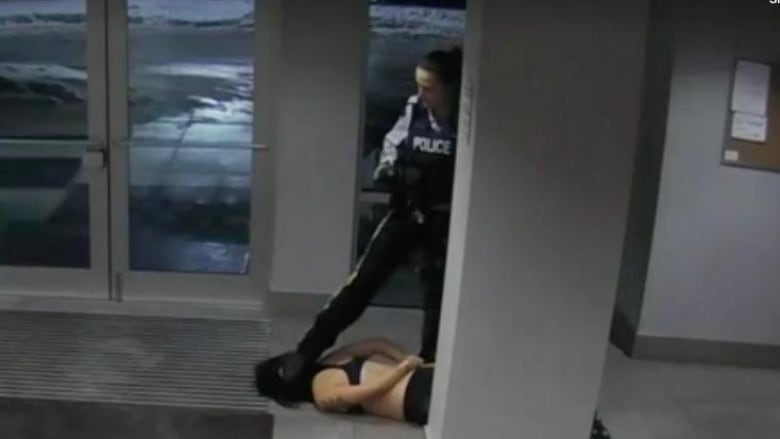 A still from a surveillance video shows a female RCMP officer stepping on a the head o of a young woman lying on the ground in an apartment lobby.