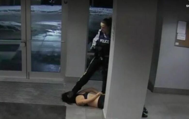 A still from a surveillance video shows a female RCMP officer stepping on a the head o of a young woman lying on the ground in an apartment lobby.