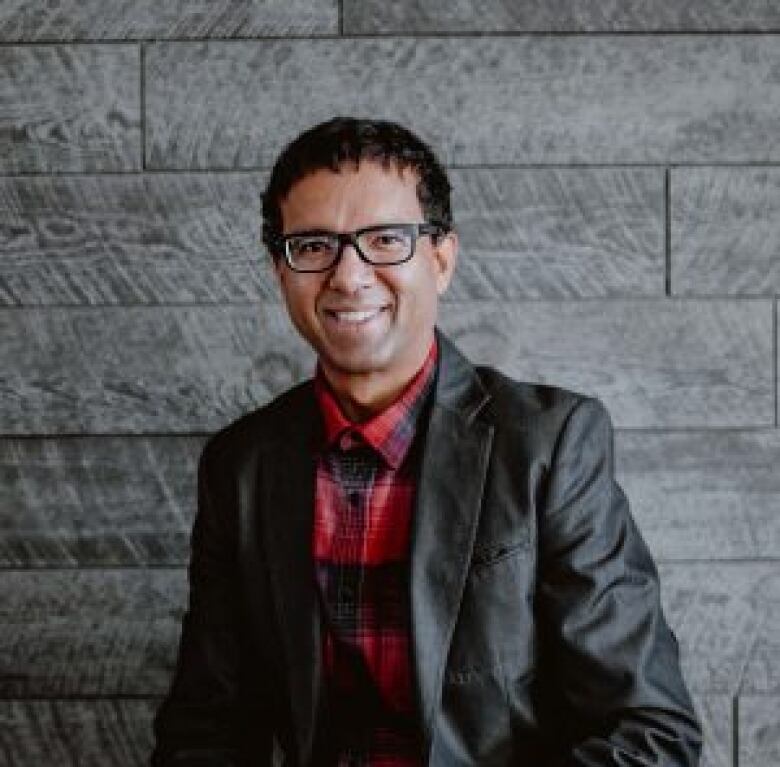 A man in a grey suit with dark hair and glasses.