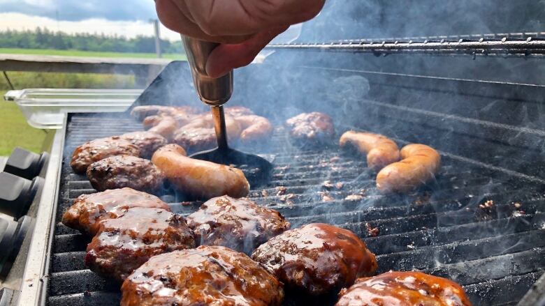 Close up of burgers and sausages on a grill, with a hand holding a spatula. 