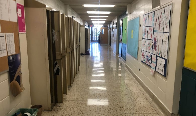 An empty school hallway with lockers on the left side and a bulletin board on the right.