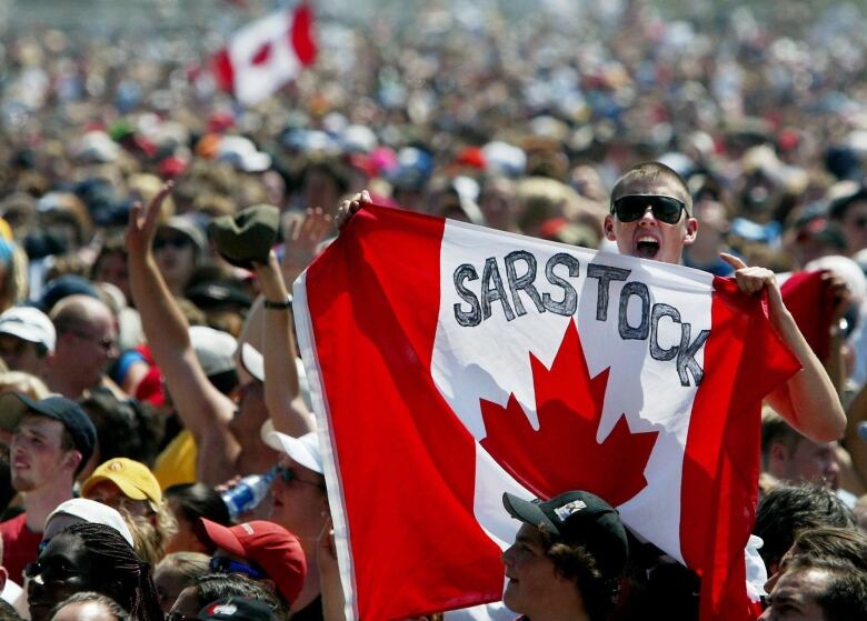 Person in crowd holds a Canadian flag with SARSTOCK written on it