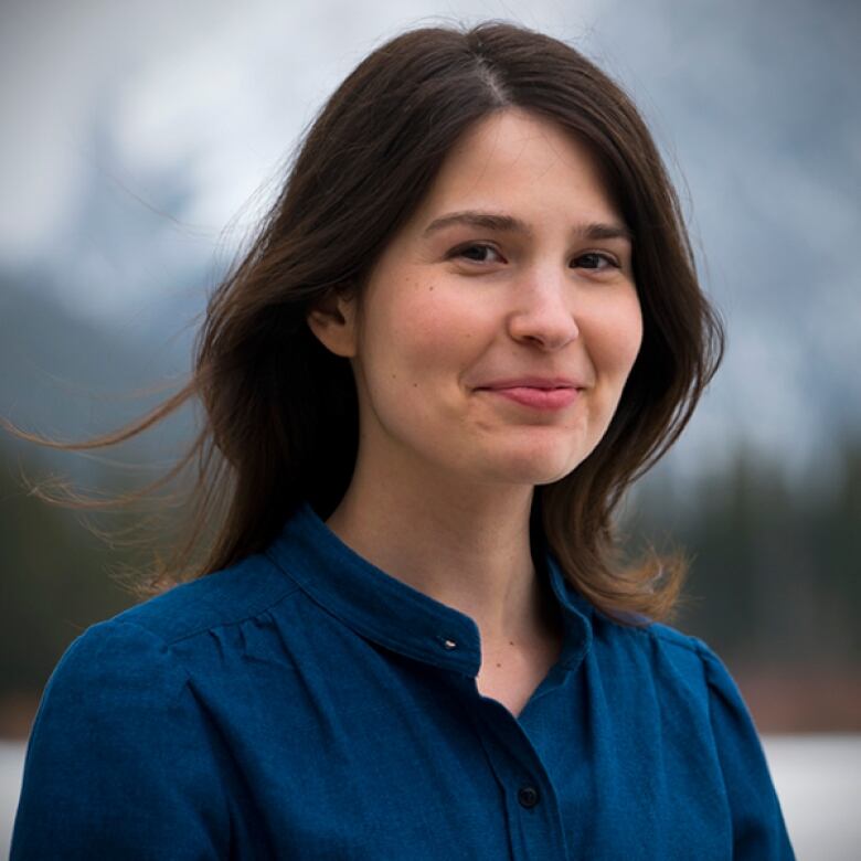 A photo of a woman with shoulder-length dark hair, wearing a blue blouse and standing outside.