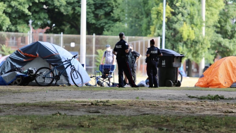 Two police officers stand beside a tent encampment in a city park