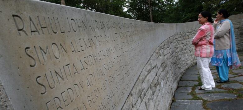 Two women look at names carved into a stone memorial wall.