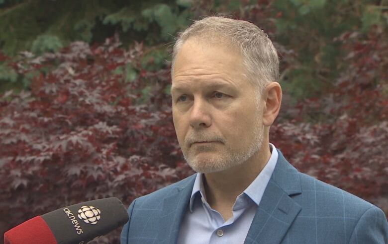 John McKiggan speaks outside while wearing a shirt and suit jacket.