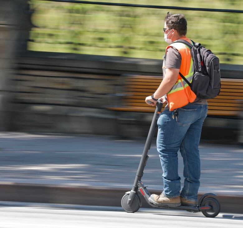 A person is riding an e-scooter and the photo has motion blur to indicate the e-scooter is in motion.