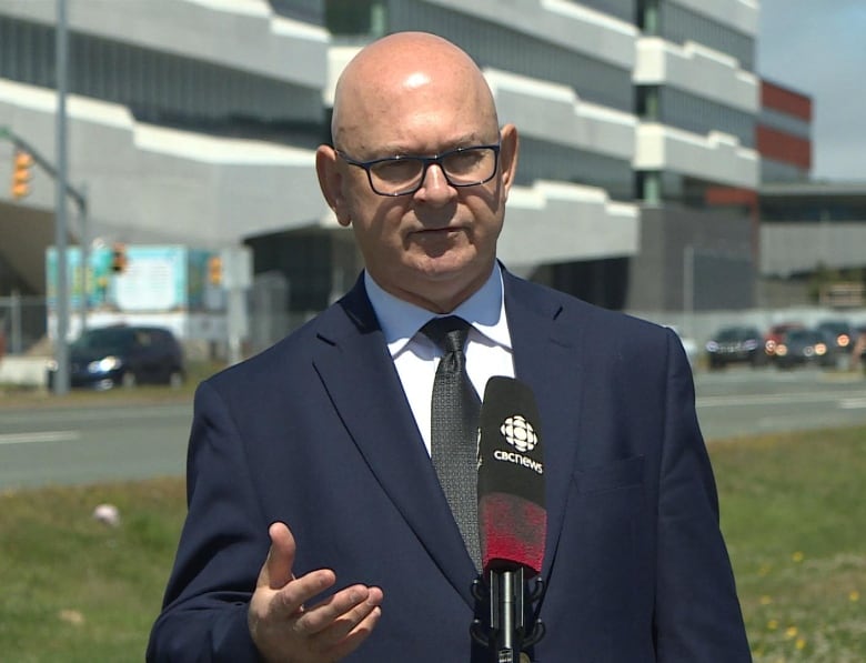 A man speaks into a CBC microphone on a sunny day. 