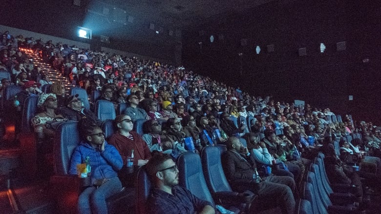 An audience watches a movie in a darkened theatre.