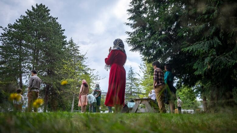 A small group of people prays in a park, with a woman in a red dress and grey hijab at centre.