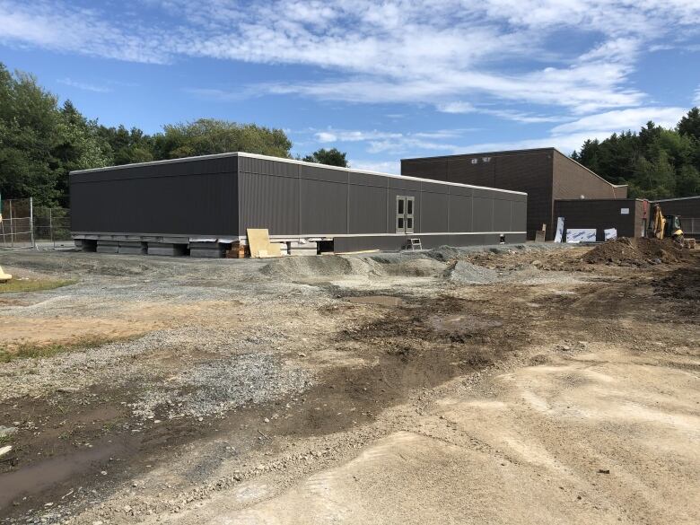 A long grey building sits on gravel.