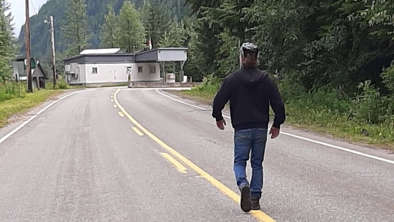 A man walks on a road towards a building.