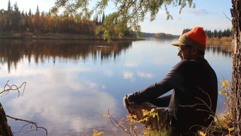 A Cree man sitting by a lake. 