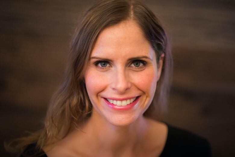 A white woman with long brown hair smiles at the camera in front of a brown background.