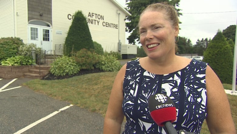 Helen Smith-MacPhail, Mayor of the Rural Municipality of West River, stands in front of Afton Community Hall.  A CBC microphone is positioned near her mouth.  