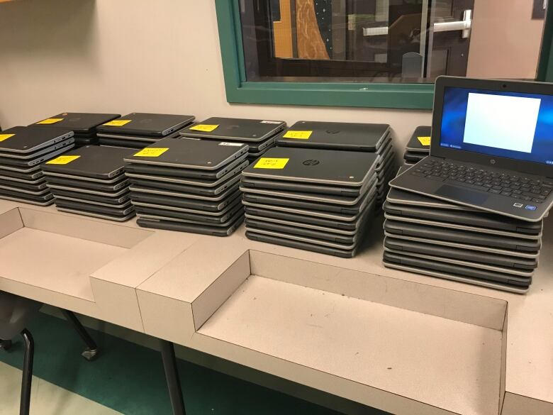 Stacks of black laptops sit on a plastic table. 