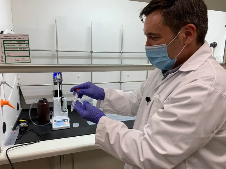 A scientist wearing a facemask handles test tubes. 