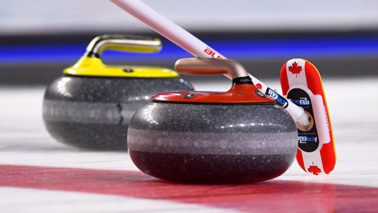 Close-up shot of a yellow and red curling rock on the ice.