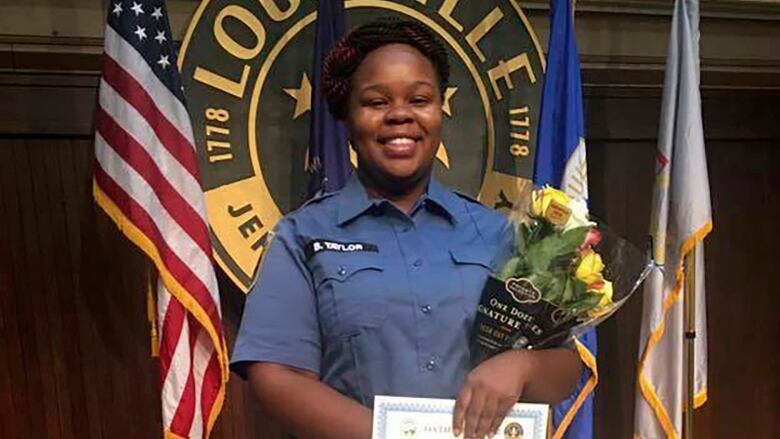 A person in uniform smiles and poses for a photograph while holding flowers and a certificate.