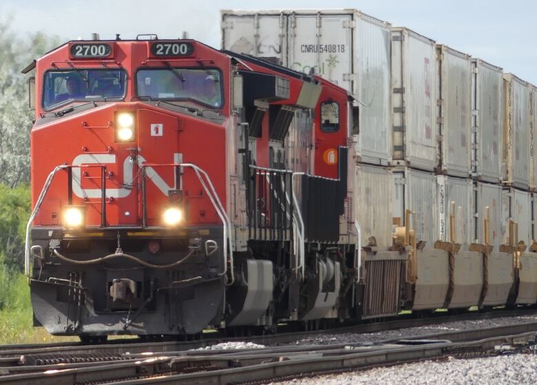 A red train, with 'CN' painted in white on front, is carrying freight cars on a railway.