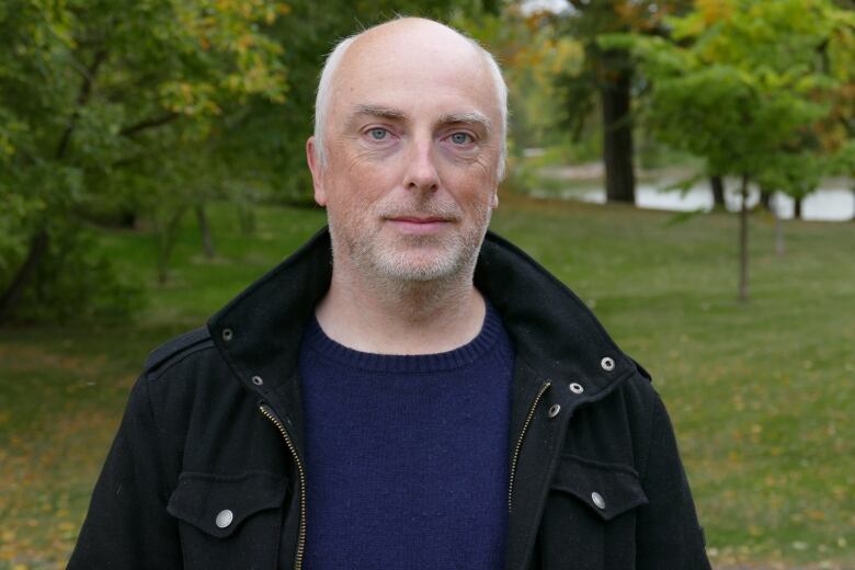 A man in a black jacket and blue sweater pose for a photo.