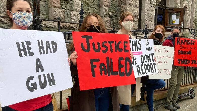 Women wearing masks hold signs outside a brick building. 