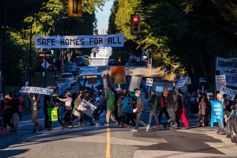 A group of protesters cross a road holding signs demanding affordable housing and housing action.