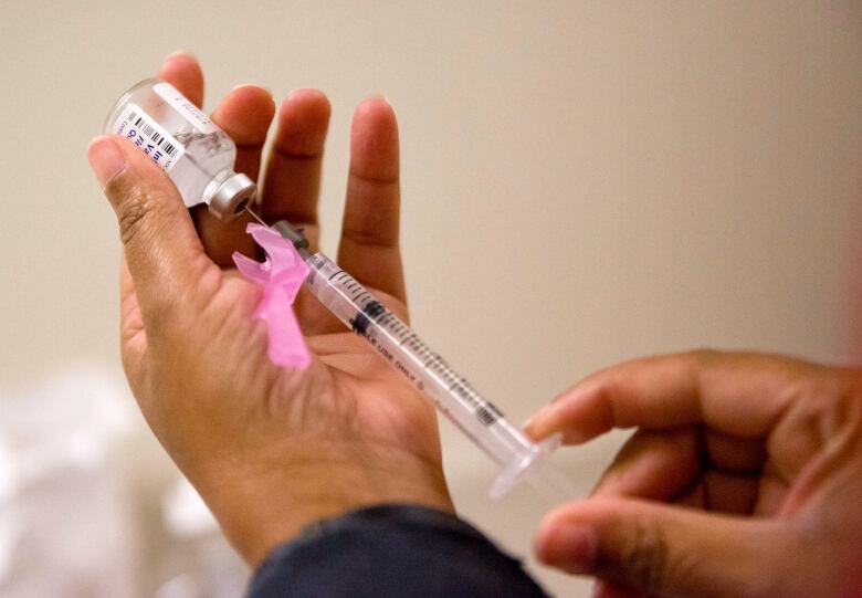 A hand holding a syringe draws vaccine from a vial held in their other hand.