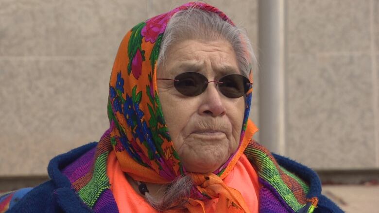 A woman with sunglasses and a head scarf stands outside.