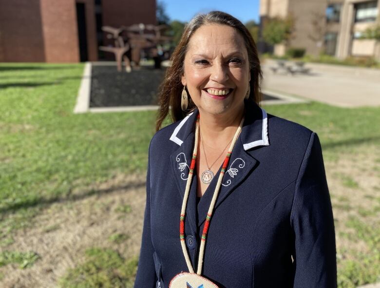 Woman wearing navy suit and Indigenous necklace smiling outside on a sunny day.