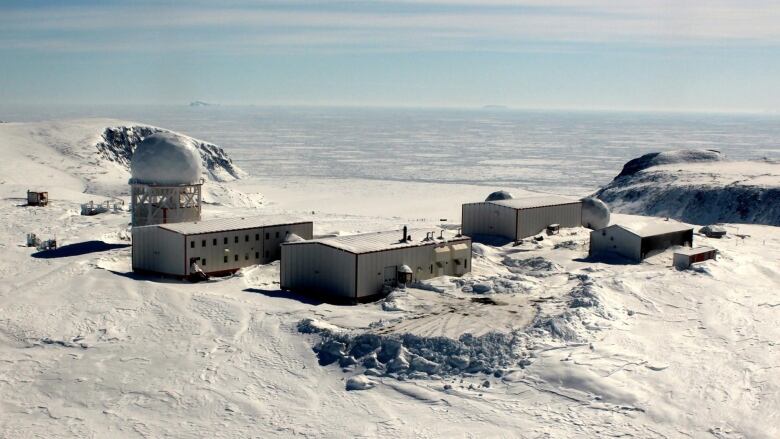 A handful of buildings on a snowy tundra with a frozen ocean in the background