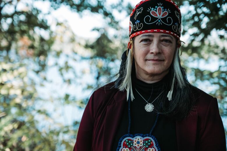 A woman wearing Indigenous regalia stands outside.