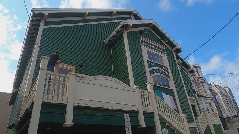 A large green building stands on a hill.