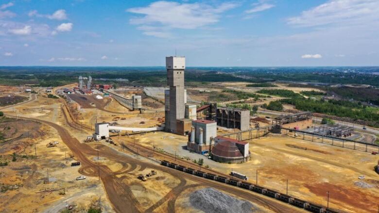 A mine shaft surrounded by mining infrastructure on a large dirt expanse under a blue, sunny sky