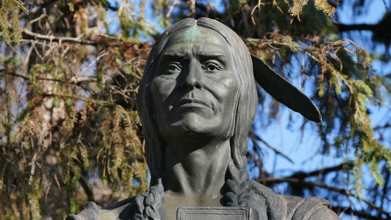 The bust of a statue of a man with braids and a feather in his hair.