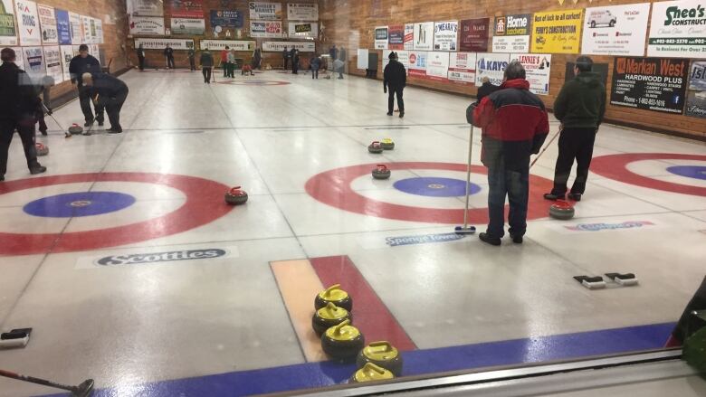 People curling on a sheet of ice with wood paneled walls surrounding them.