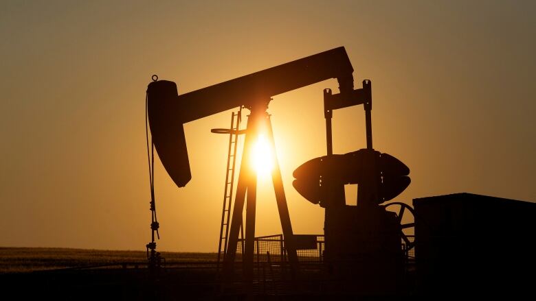 A silhouette of oil pump jack sits on the prairie, with the sun behind. 